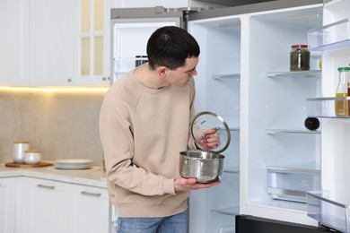 Photo of Man with pot near empty refrigerator in kitchen