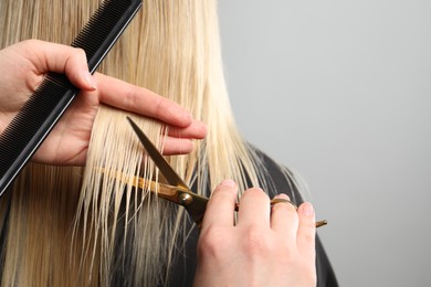 Photo of Hairdresser cutting client's hair with scissors on light grey background, closeup. Space for text
