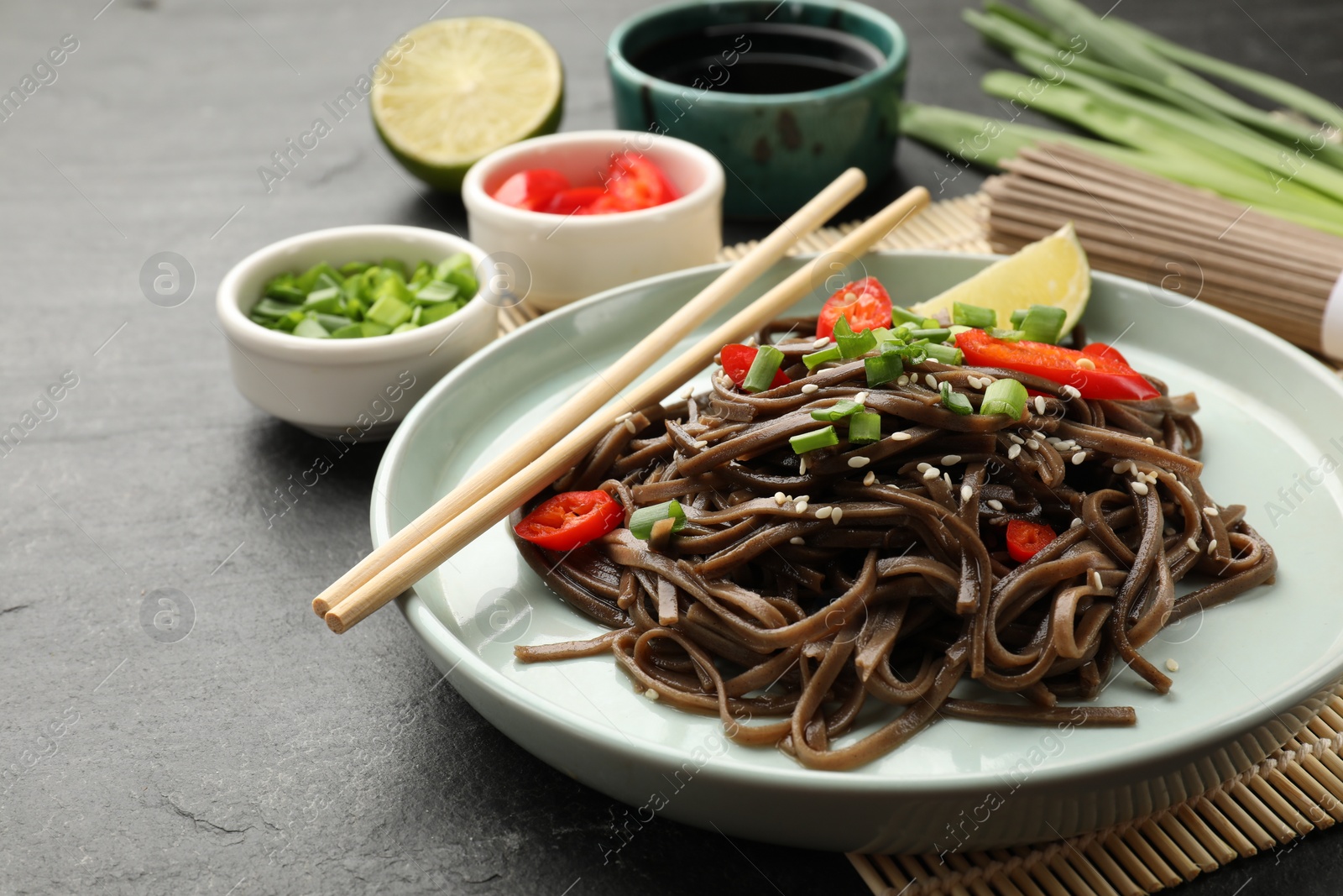 Photo of Tasty buckwheat noodles (soba) with chili pepper, onion and chopsticks on grey table, closeup