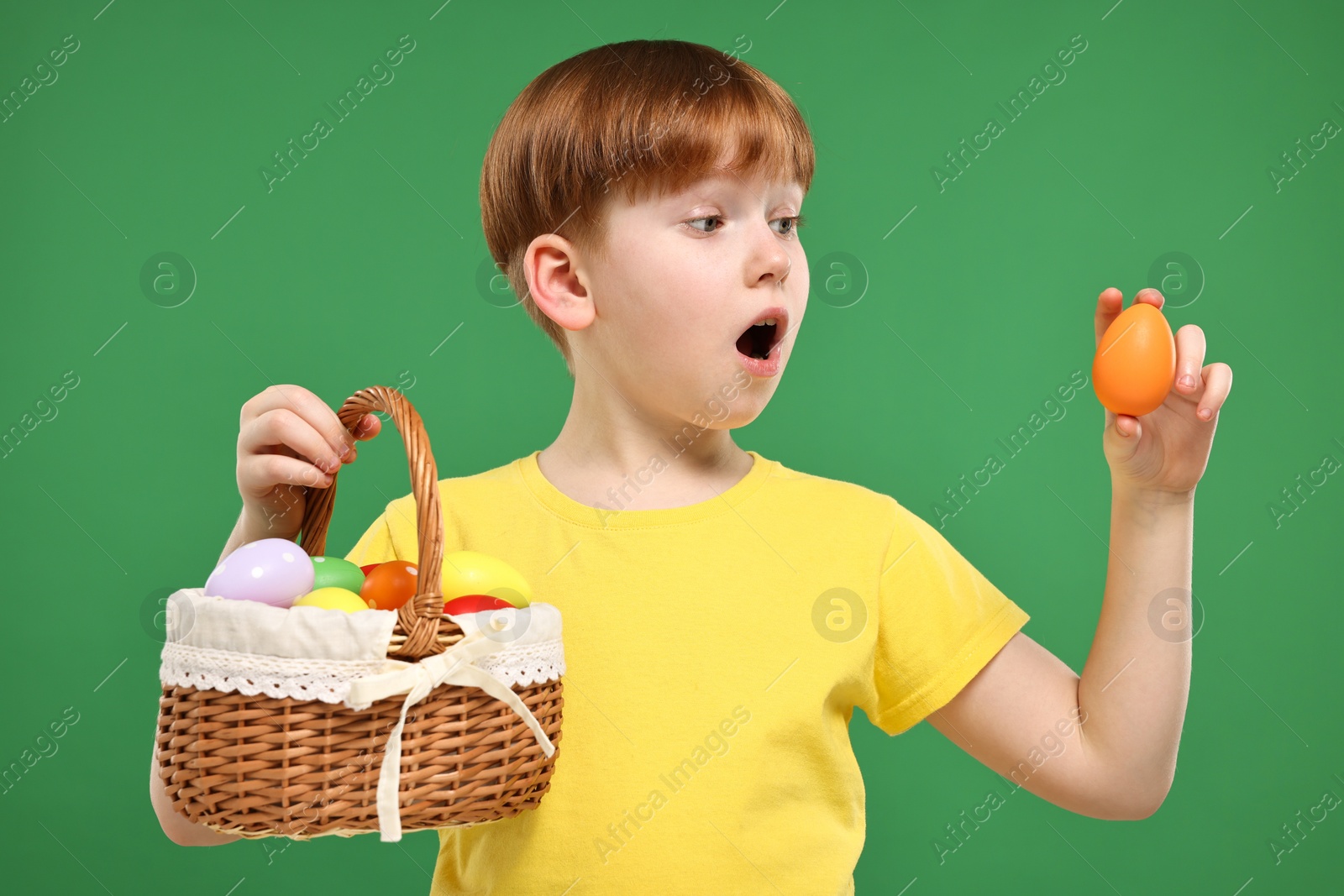 Photo of Easter celebration. Surprised little boy with painted eggs on green background