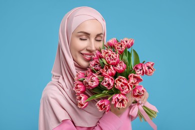 Happy woman in hijab with beautiful bouquet on light blue background