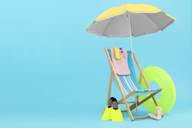 Photo of Deck chair, umbrella and beach accessories against light blue background, space for text. Summer vacation