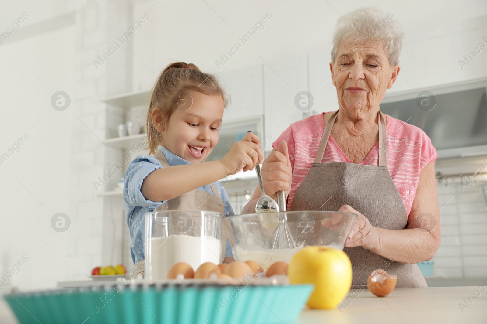 Photo of Cute girl and her grandmother cooking in kitchen