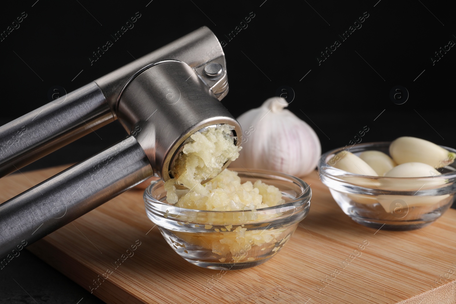 Photo of Crushing garlic with press into bowl at wooden table, closeup