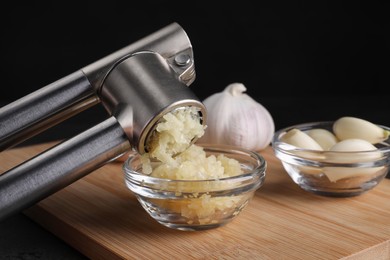 Crushing garlic with press into bowl at wooden table, closeup