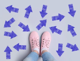 Image of Choosing future profession. Girl standing in front of drawn signs on grey background, top view. Arrows pointing in different directions symbolizing diversity of opportunities