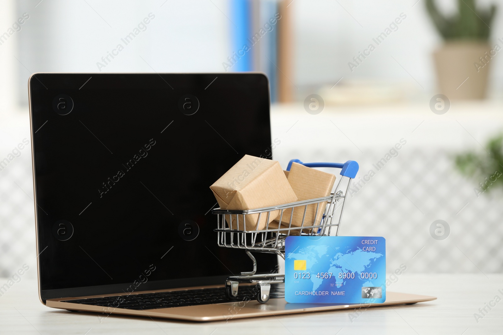 Photo of Online payment concept. Small shopping cart with bank card, boxes and laptop on white table