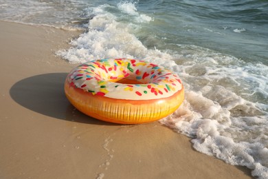 Photo of Inflatable ring with doughnut pattern on sandy beach near sea