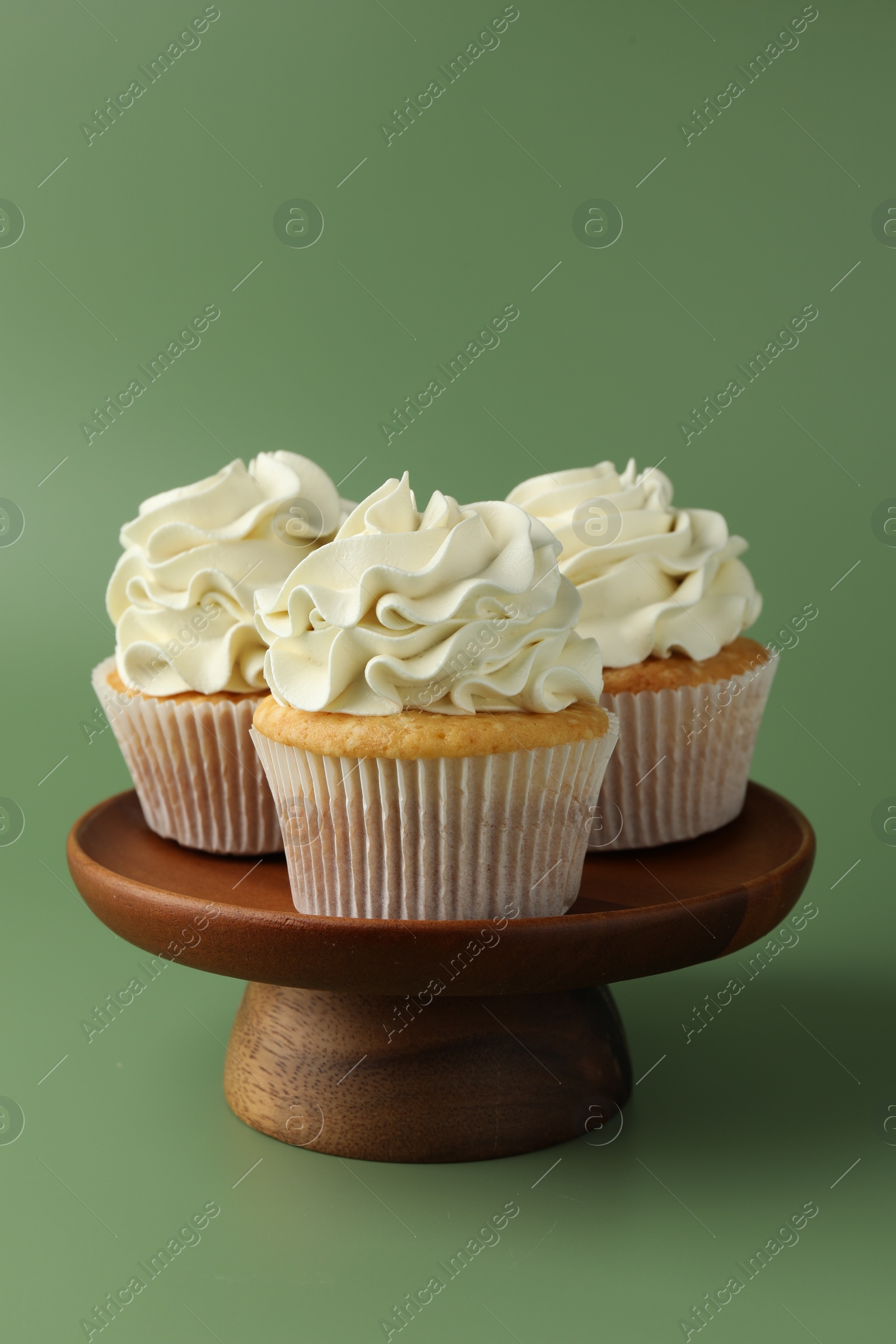 Photo of Tasty vanilla cupcakes with cream on green background