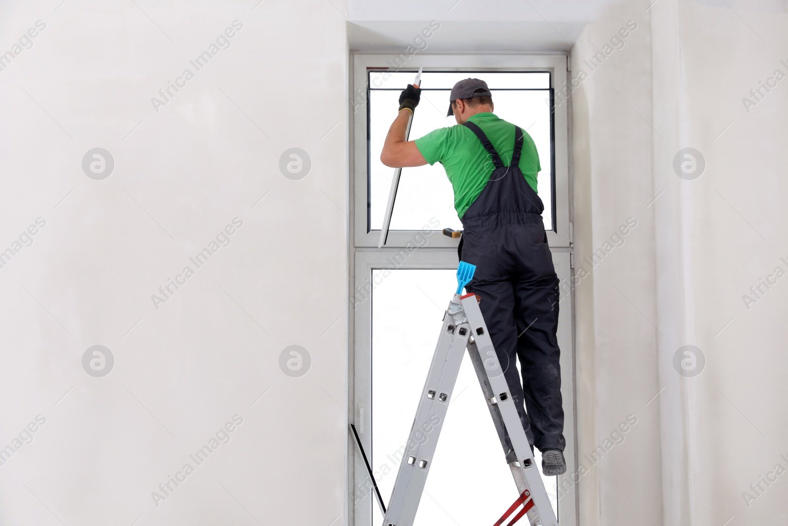 Photo of Worker in uniform installing double glazing window indoors, back view