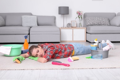 Photo of Tired woman sleeping on floor after cleaning carpet at home