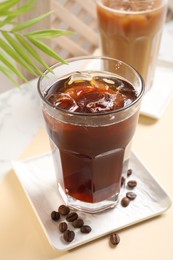 Photo of Refreshing iced coffee in glass on beige table, closeup