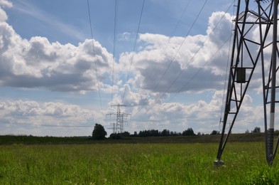 Modern high voltage towers in field on sunny day