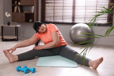 Photo of Overweight mature woman stretching on yoga mat at home
