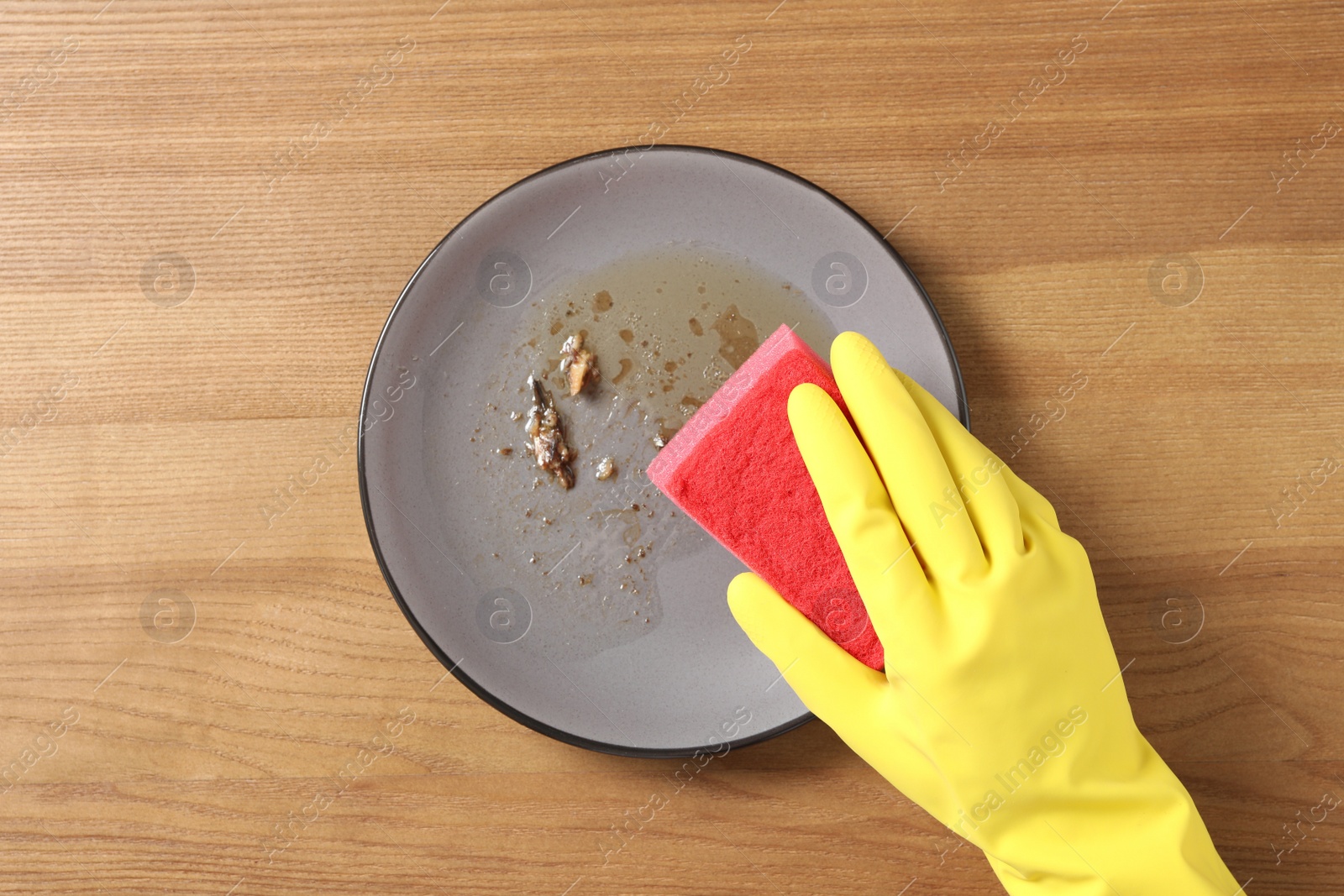 Photo of Woman washing dirty plate at wooden table, top view