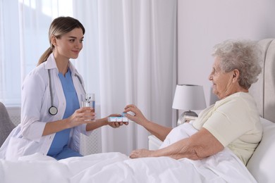 Photo of Young caregiver giving medication to senior woman in bedroom. Home health care service