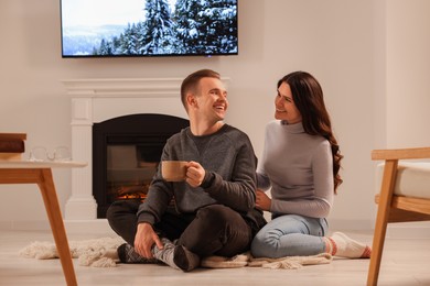 Photo of Happy lovely couple with hot drinks spending time together near fireplace at home
