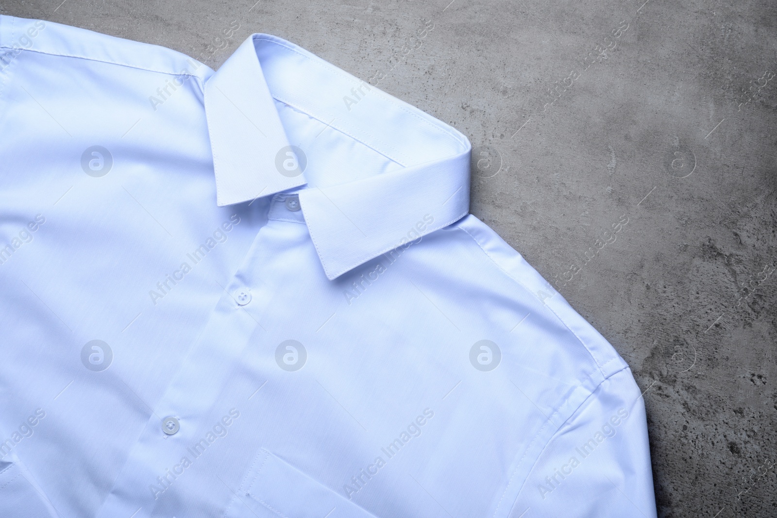 Photo of Stylish white shirt on grey stone table, top view. Dry-cleaning service