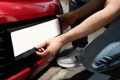 Photo of Man installing vehicle registration plate outdoors, closeup