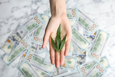 Photo of Woman holding hemp leaf over money on table, top view