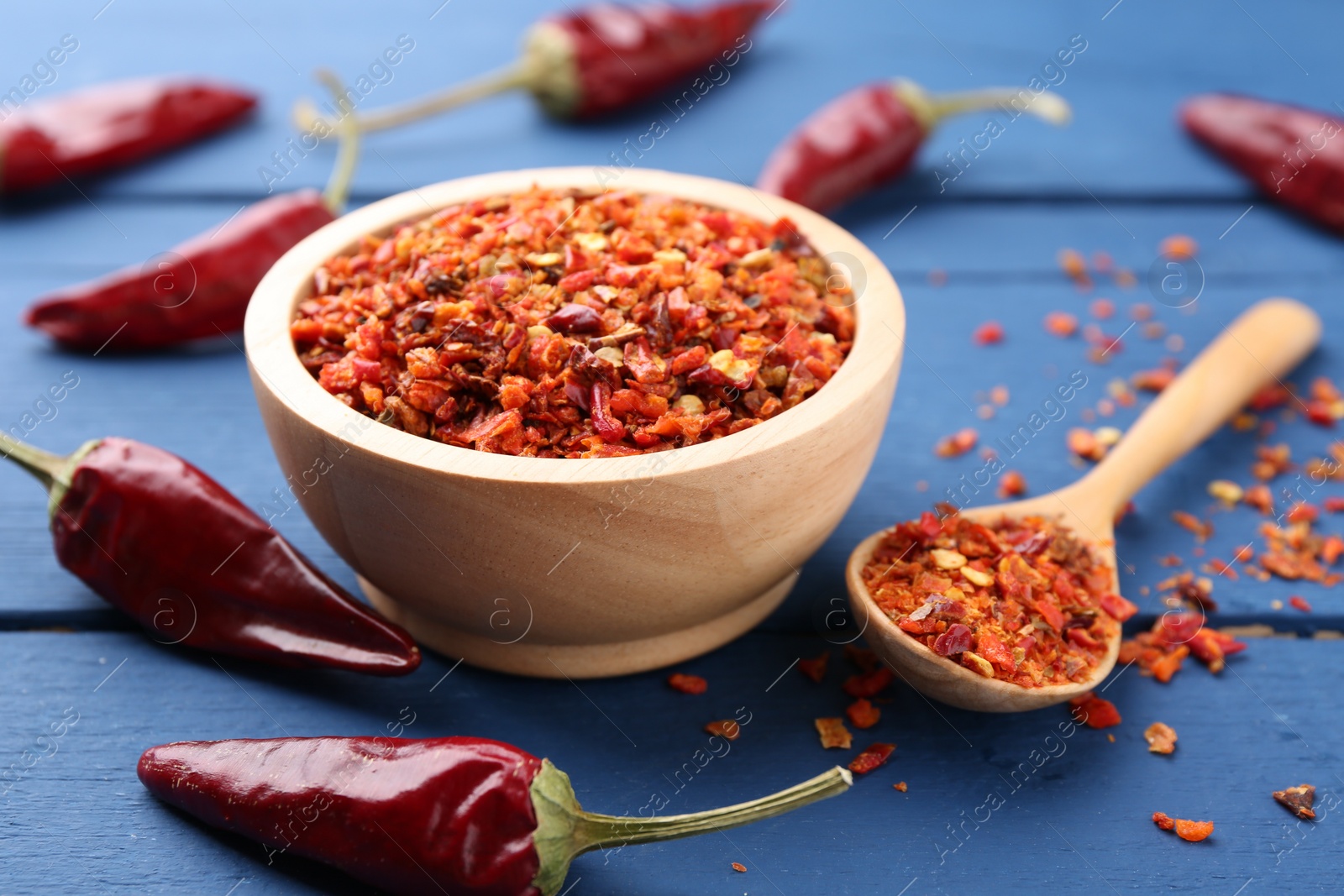 Photo of Chili pepper flakes and pods on blue wooden table, closeup