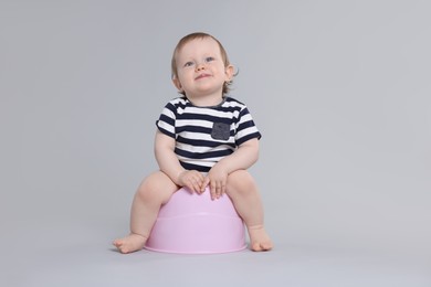 Photo of Little child sitting on baby potty against light grey background