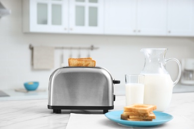 Photo of Modern toaster with slices of bread and milk on white marble table in kitchen