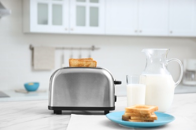 Modern toaster with slices of bread and milk on white marble table in kitchen