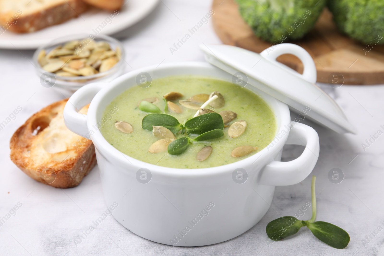 Photo of Delicious broccoli cream soup with pumpkin seeds on white marble table