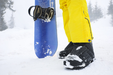 Photo of Young woman with snowboard wearing winter sport clothes outdoors, closeup