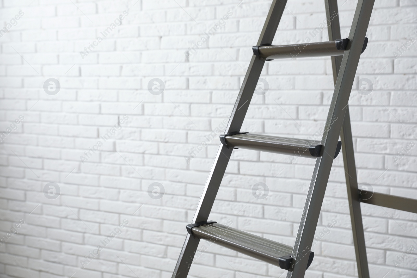 Photo of Metal stepladder near white brick wall, closeup. Space for text