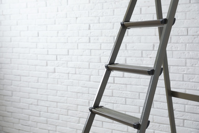 Metal stepladder near white brick wall, closeup. Space for text