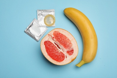 Photo of Condoms with banana and cut grapefruit on light blue background, flat lay. Safe sex