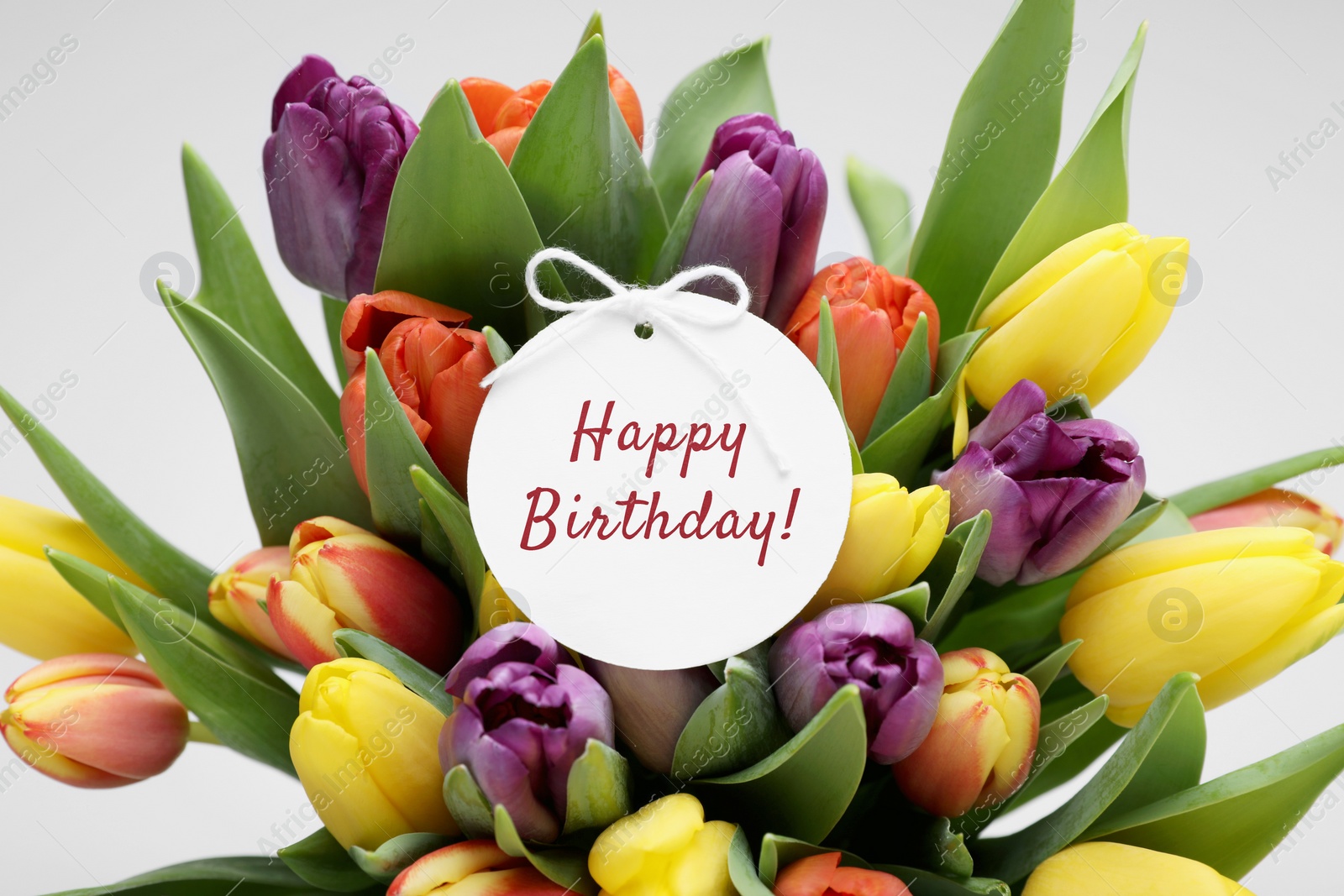 Image of Beautiful bouquet of tulips with Happy Birthday card on light background, closeup