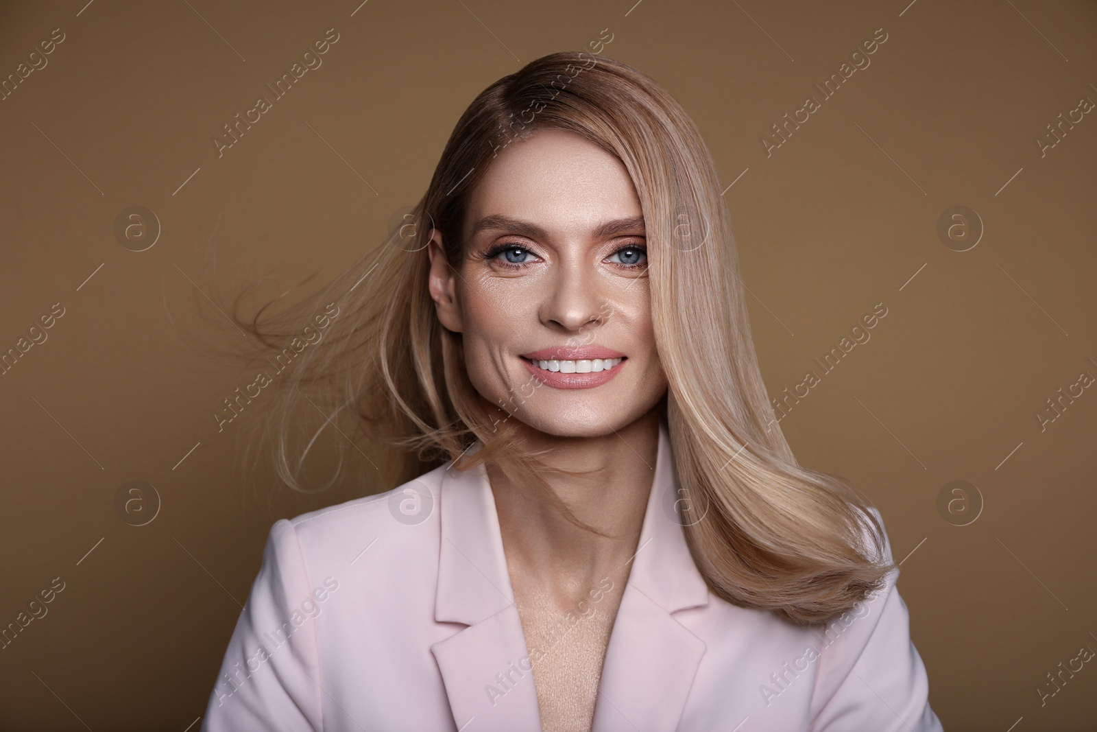 Image of Portrait of stylish attractive woman with blonde hair smiling on pastel brown background