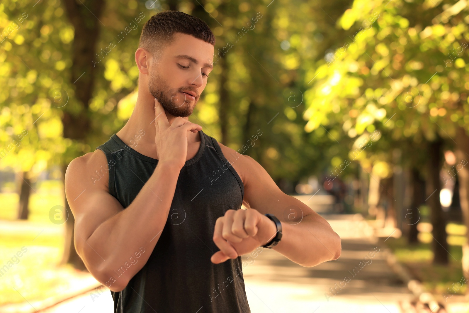 Photo of Attractive serious man checking pulse after training in park on sunny day. Space for text