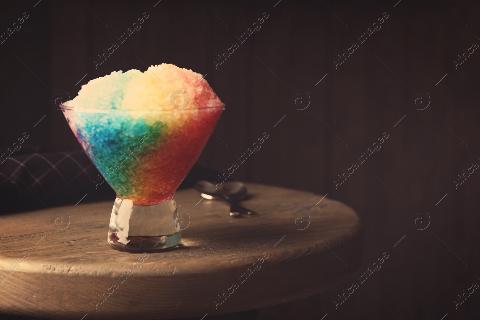 Photo of Rainbow shaving ice in glass dessert bowl on wooden table indoors