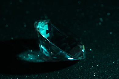 Photo of Beautiful dazzling diamond on green glitter surface, closeup