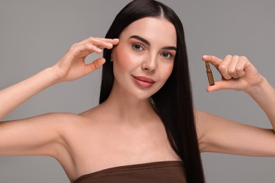 Beautiful young woman holding skincare ampoule on grey background