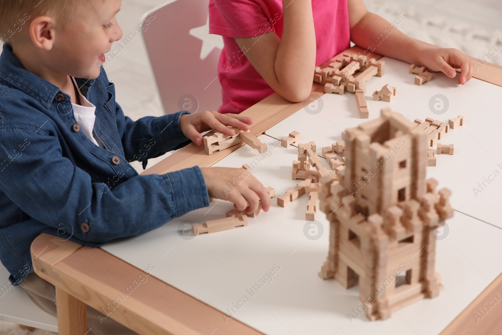 Photo of Little boy and girl playing with wooden tower at table indoors, closeup. Children's toy