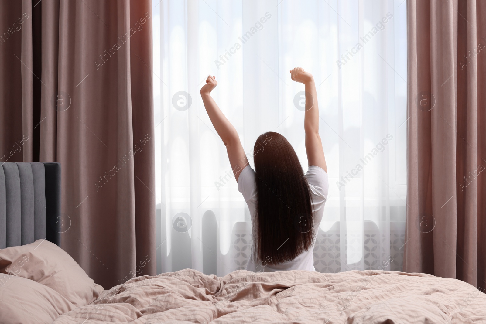 Photo of Woman stretching on bed at home, back view. Lazy morning