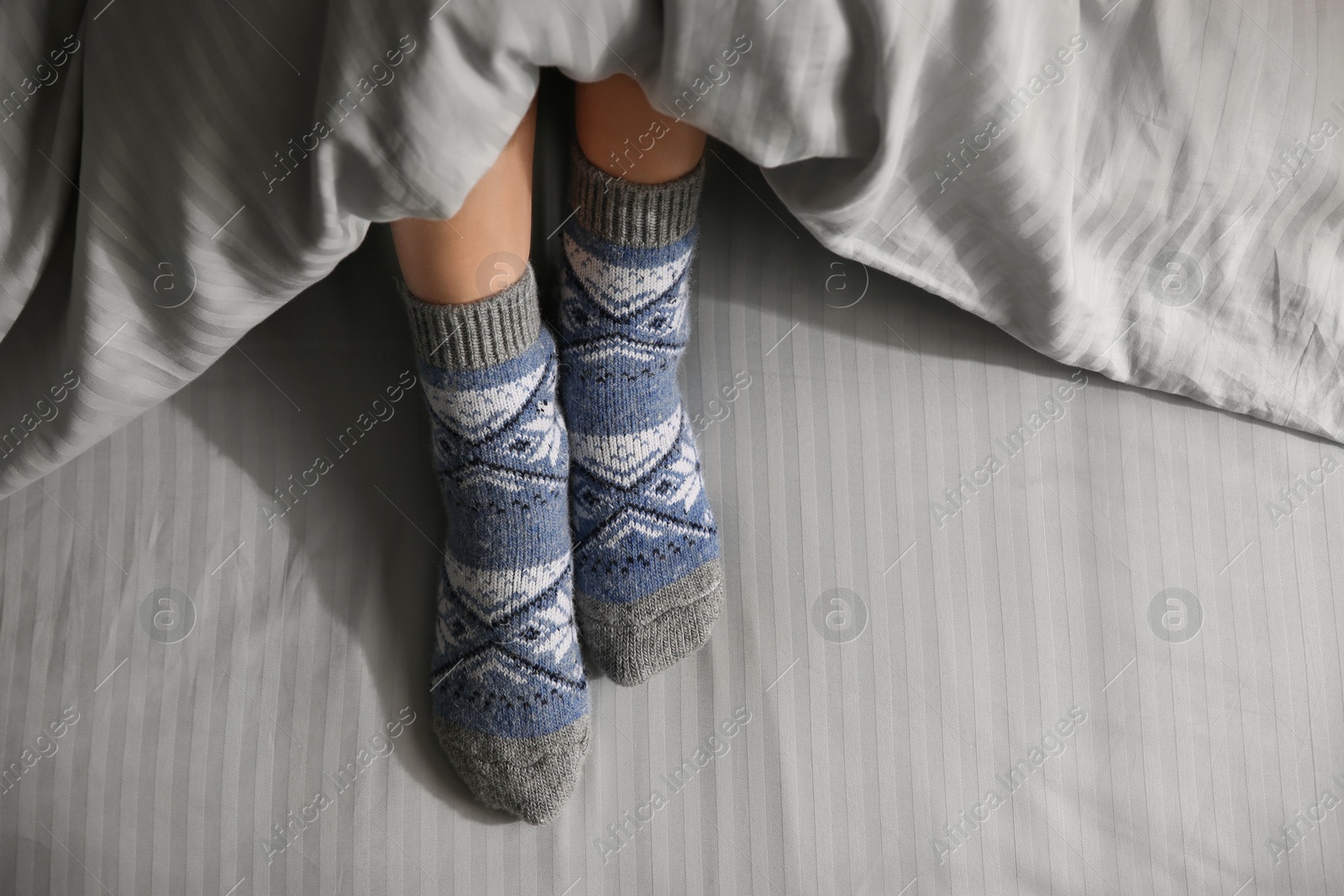 Photo of Woman wearing knitted socks under blanket in bed, top view