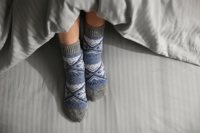 Photo of Woman wearing knitted socks under blanket in bed, top view