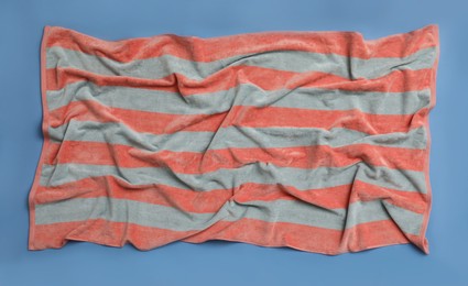 Photo of Crumpled striped beach towel on blue background, top view