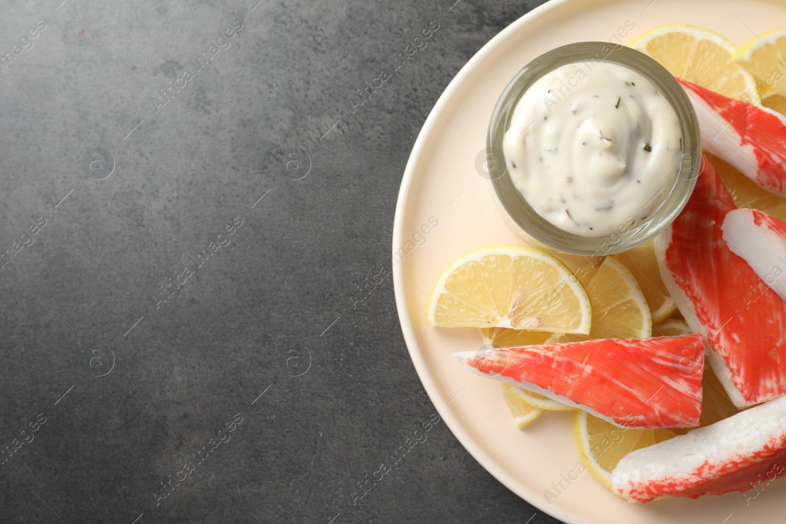 Photo of Delicious crab sticks with lemon slices and sauce on grey table, top view. Space for text