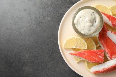 Photo of Delicious crab sticks with lemon slices and sauce on grey table, top view. Space for text