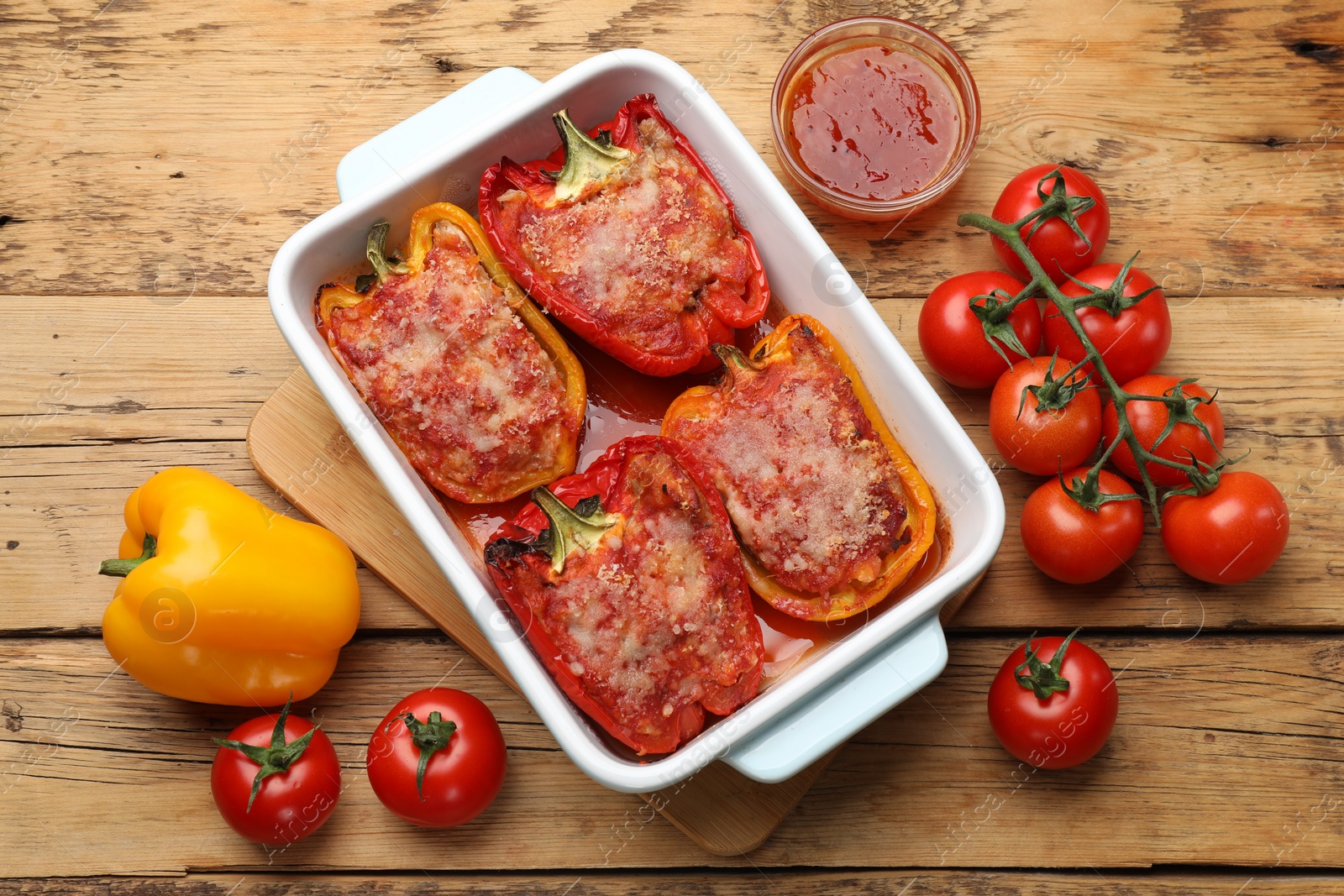 Photo of Tasty stuffed peppers in dish and ingredients on wooden table, flat lay