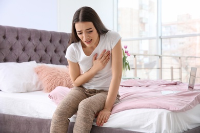 Photo of Young woman suffering from heart attack on bed at home