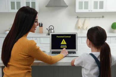 Photo of Mother installing parental control on laptop in kitchen, back view. Child safety