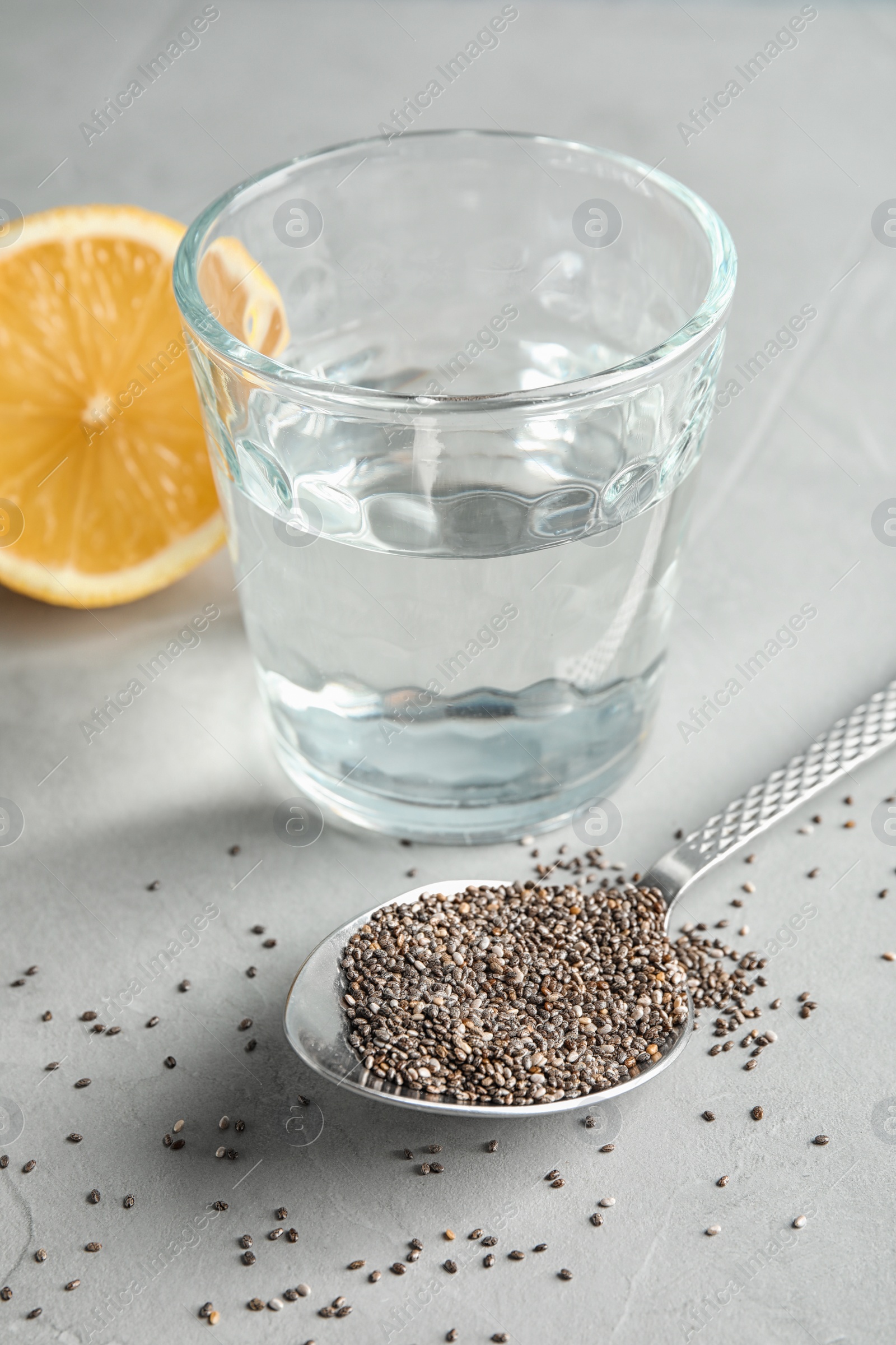 Photo of Spoon with chia seeds and glass of water on grey background